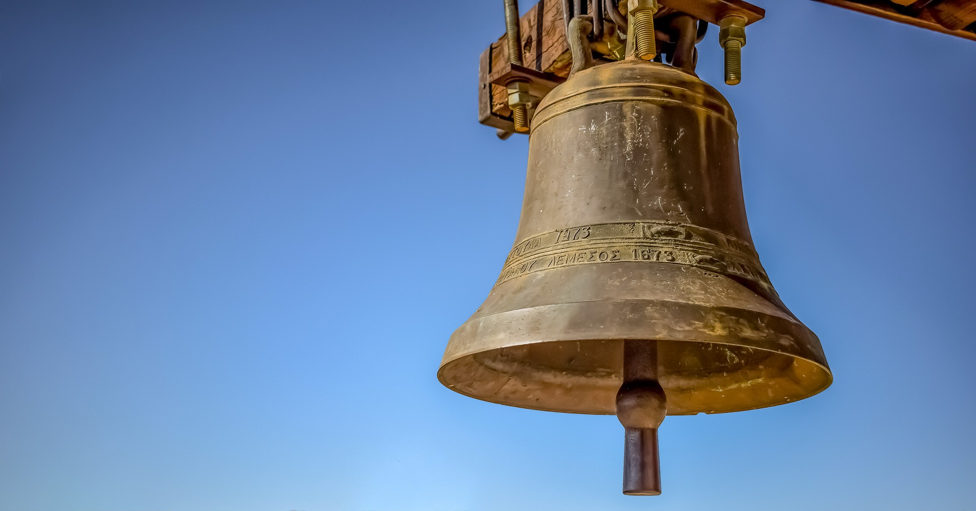 picture of large bronze bell against blue sky with Greek lettering